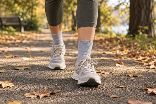 Walker wearing light grey crew socks and neutral sneakers on an autumn park path; illustrative scene, not MP product photography
