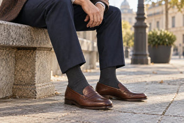 Charcoal crew socks worn with brown penny loafers and navy trousers on a city bench; illustrative scene, not MP product photography